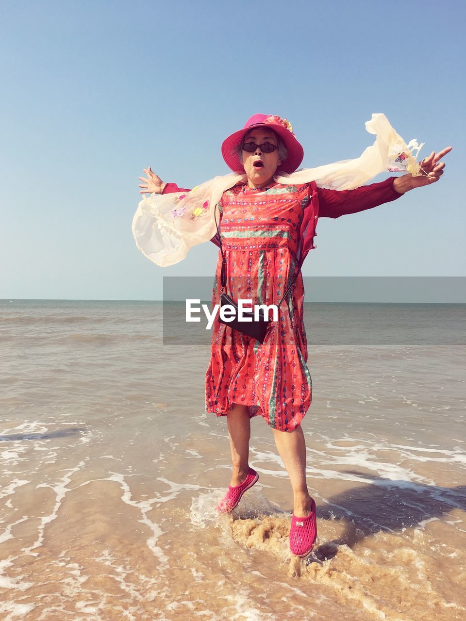 Senior woman jumping at beach against sky