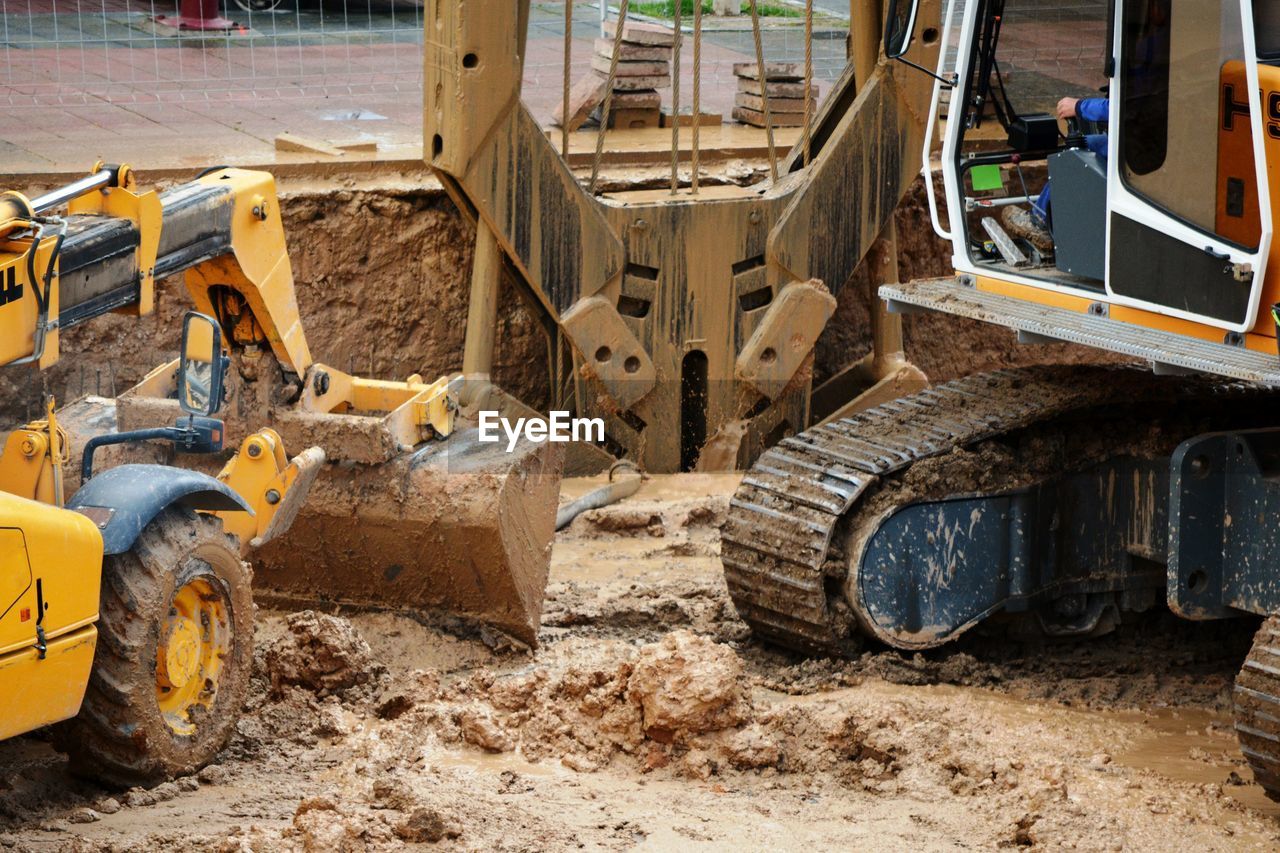 A yellow digger excavating mud and one crane bucket picking up