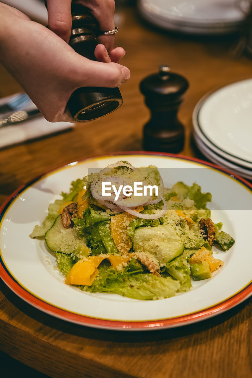 Cropped hands seasoning food in plate on table