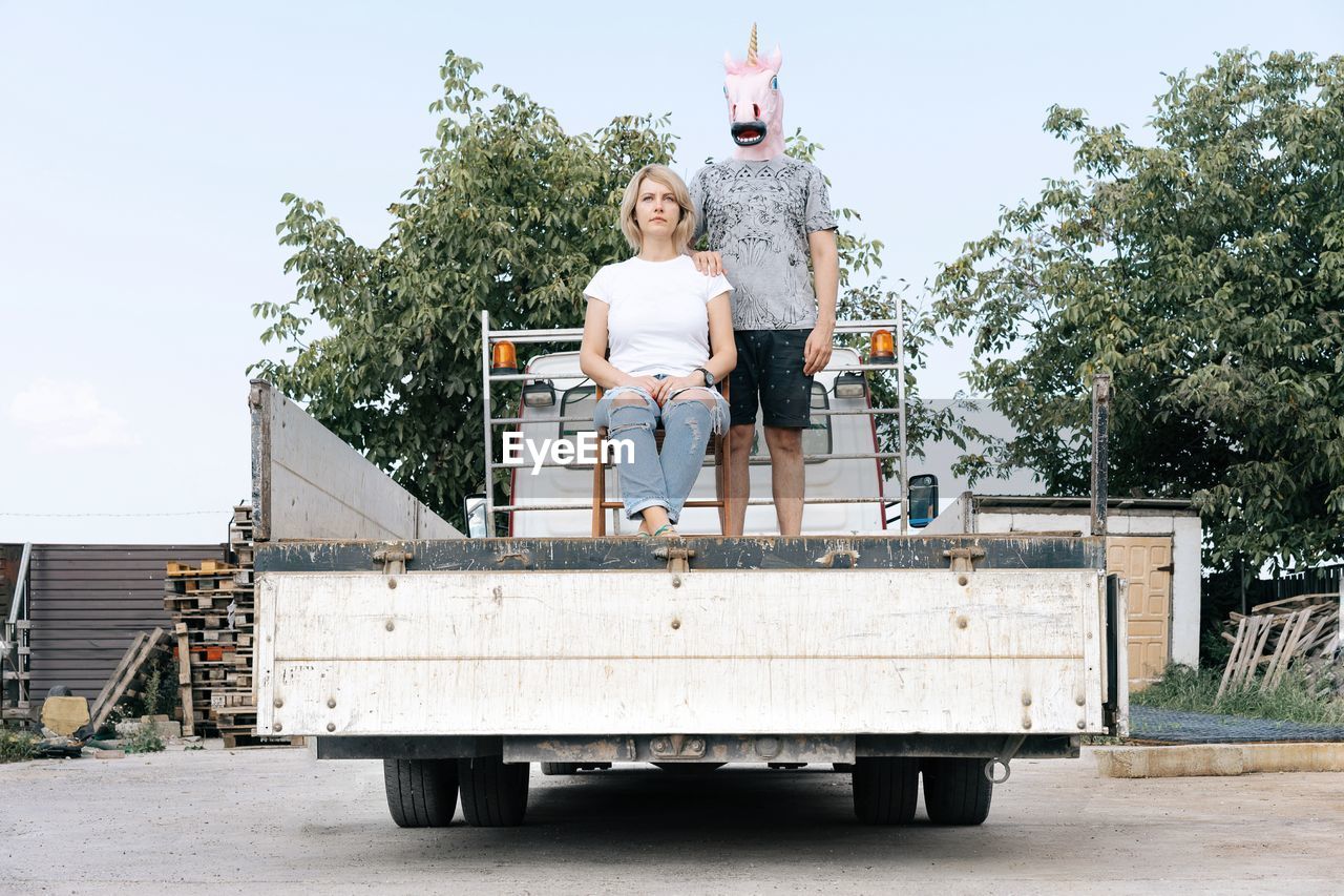 Man wearing horse mask standing by woman in truck