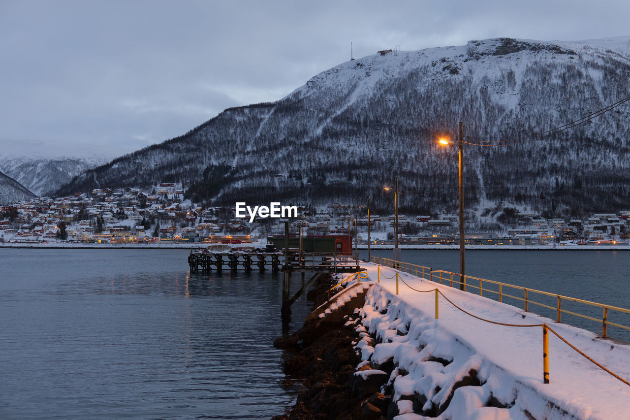 Illuminated light on jetty in fjord against mountain at dawn
