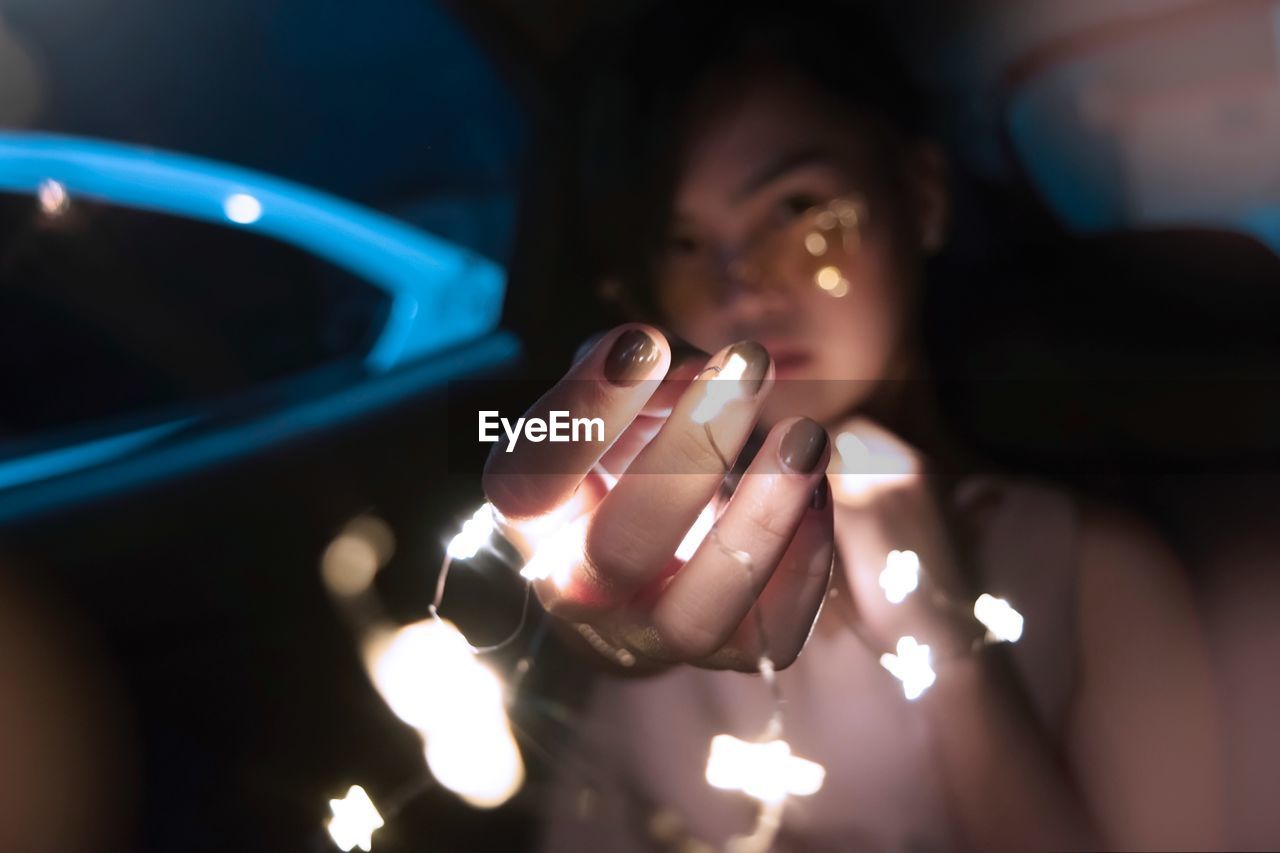 Portrait of woman holding illuminated string lights in darkroom