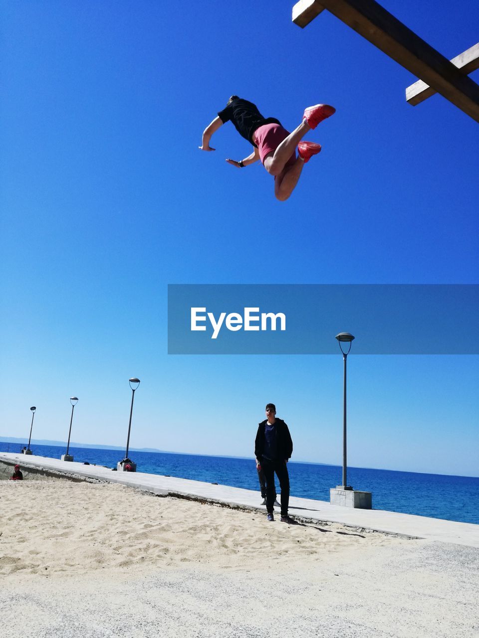 FULL LENGTH OF MAN PARAGLIDING AT BEACH AGAINST CLEAR SKY