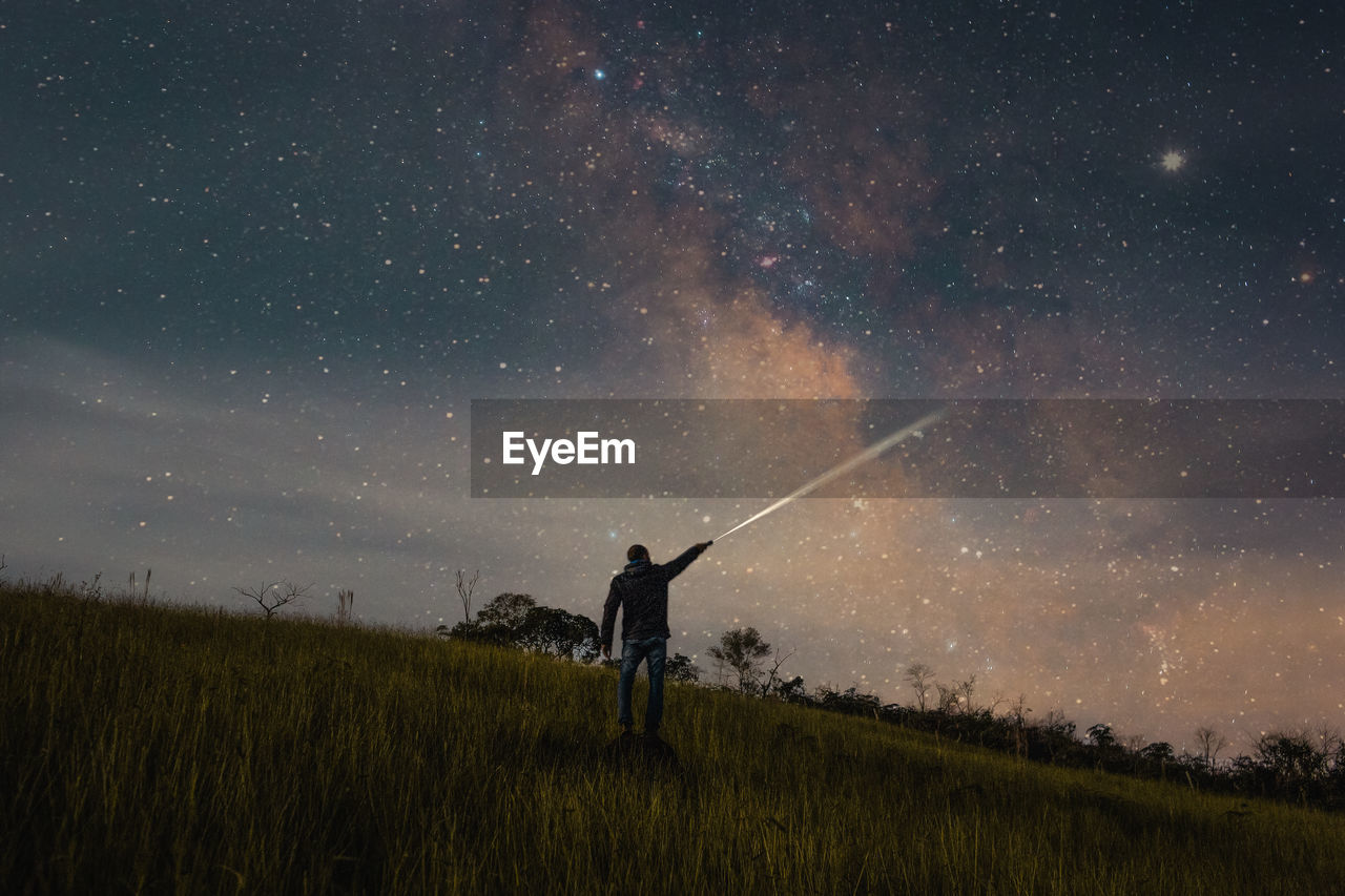 Rear view of man holding flashlight on land against star field