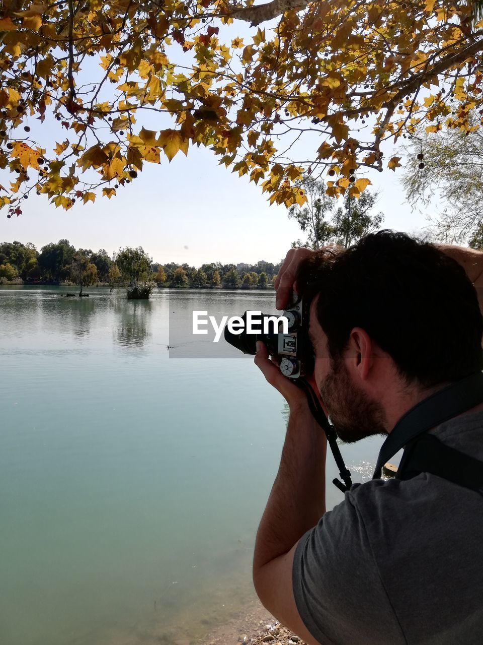 Portrait of man photographing by lake