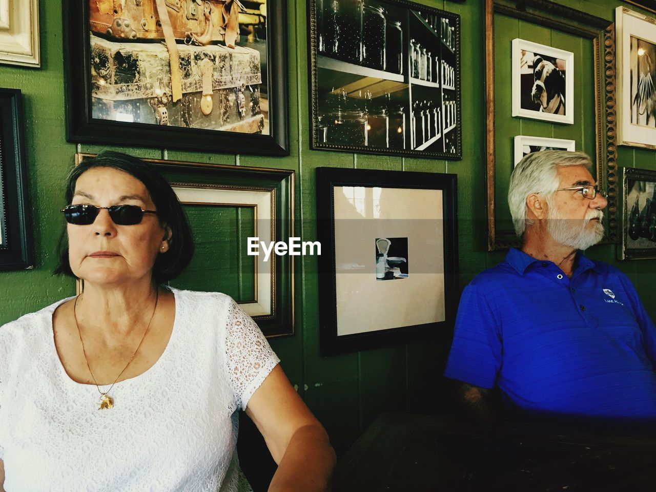Senior man and woman looking away while sitting against picture frames on wall