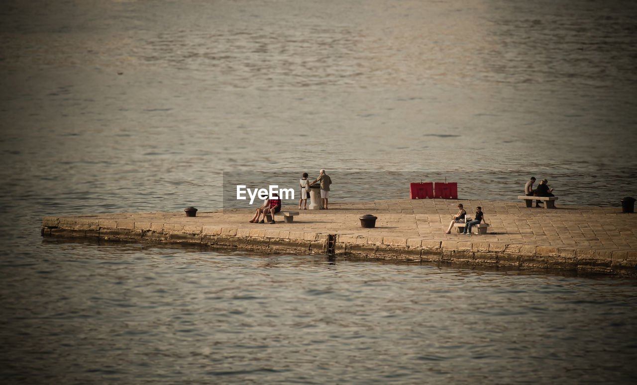 Mid distant view of people relaxing at harbor by sea