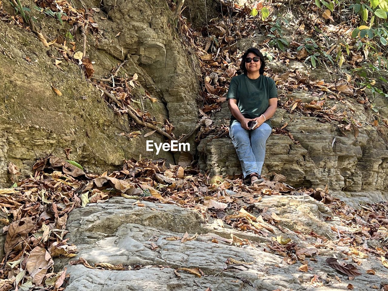 one person, full length, leisure activity, nature, casual clothing, front view, lifestyles, wilderness, day, land, rock, young adult, tree, geology, forest, adult, plant, looking at camera, outdoors, men, portrait, soil, standing, autumn, high angle view, sunlight, trail, sitting, person, walking, clothing