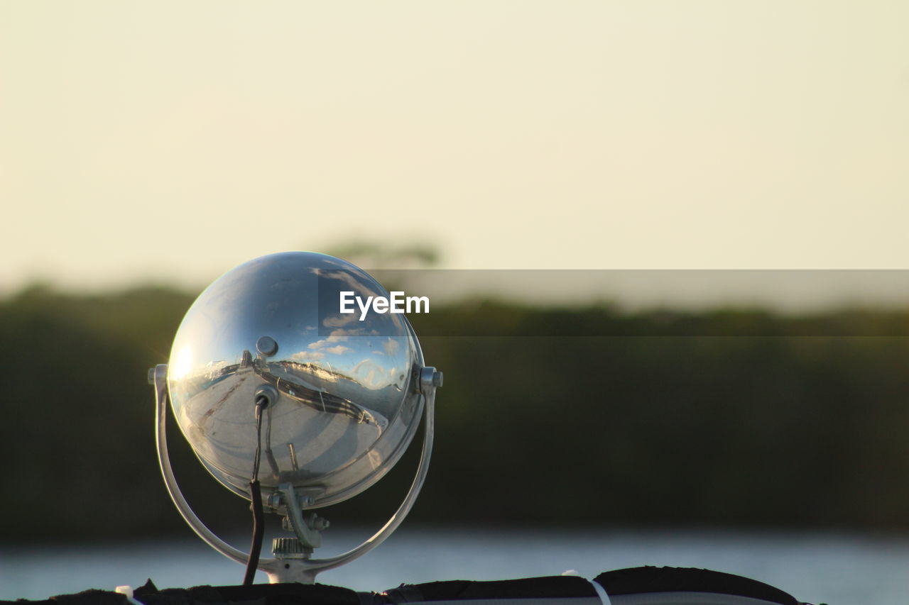 CLOSE-UP OF CRYSTAL BALL ON METAL AGAINST SKY