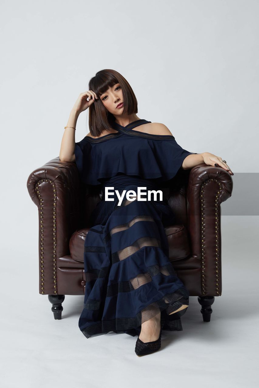 Portrait of woman sitting on chair against white background