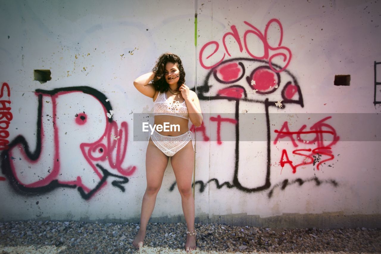 Full length of seductive woman standing against graffiti wall