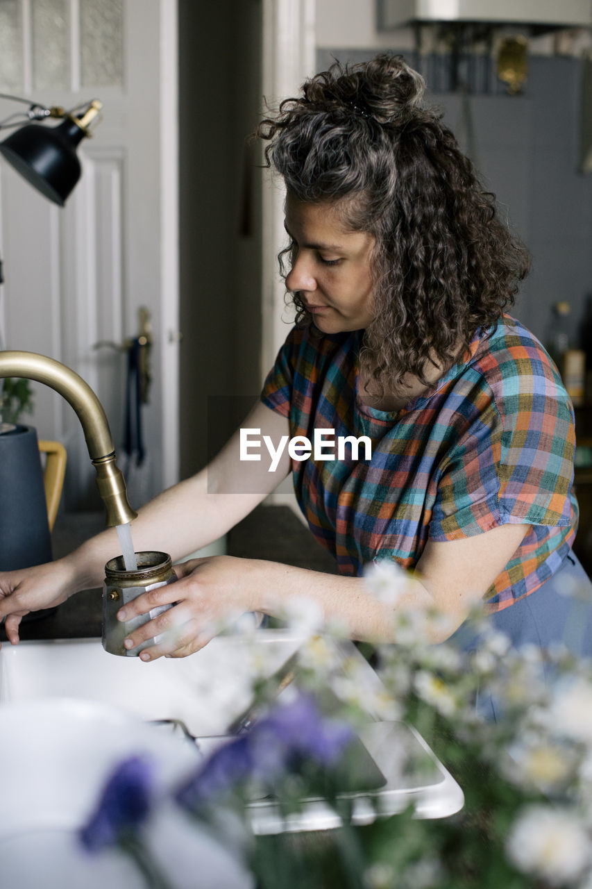 Woman filling water in coffee pot through faucet at home