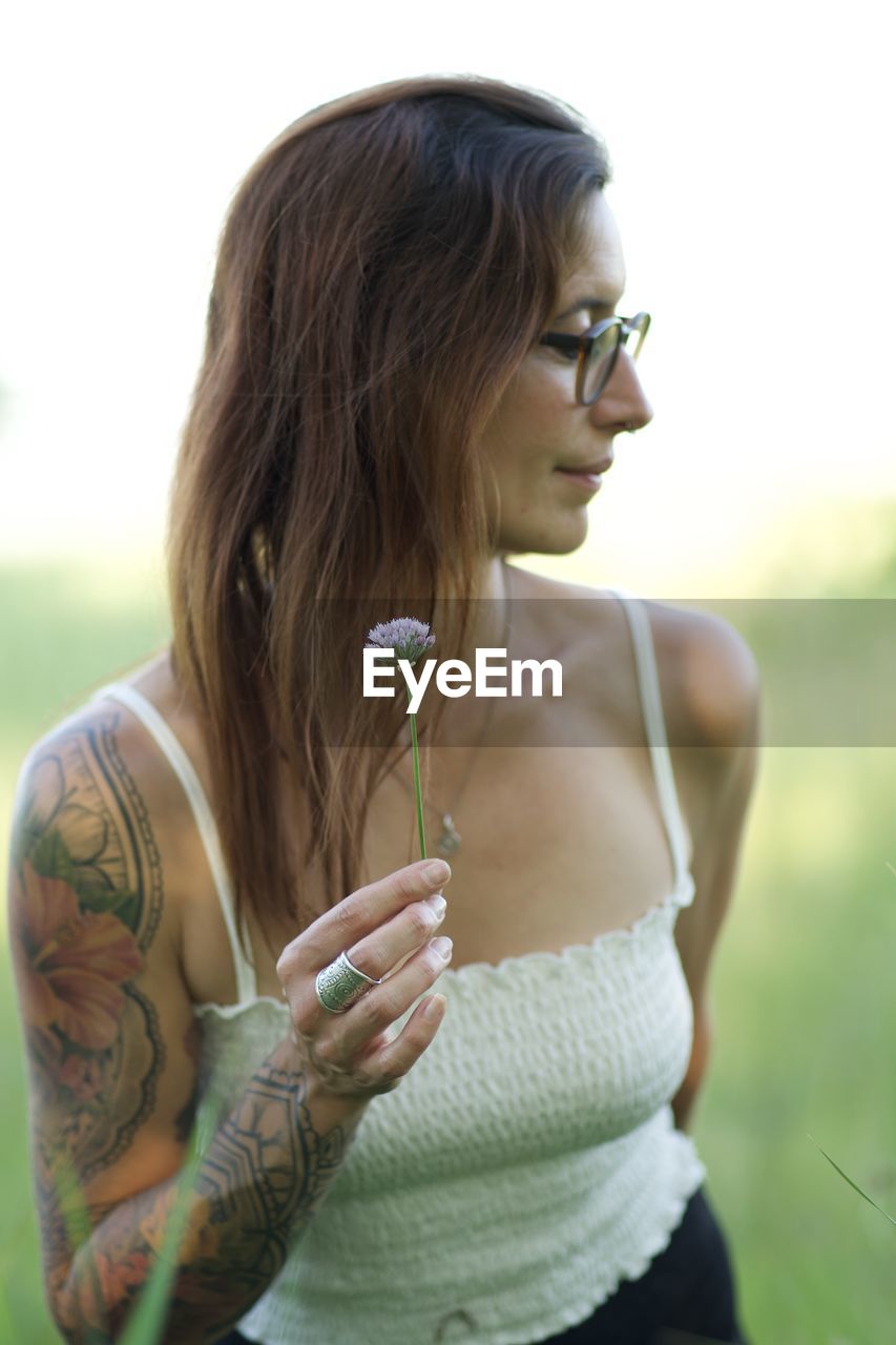 Portrait of young woman holding camera while standing outdoors