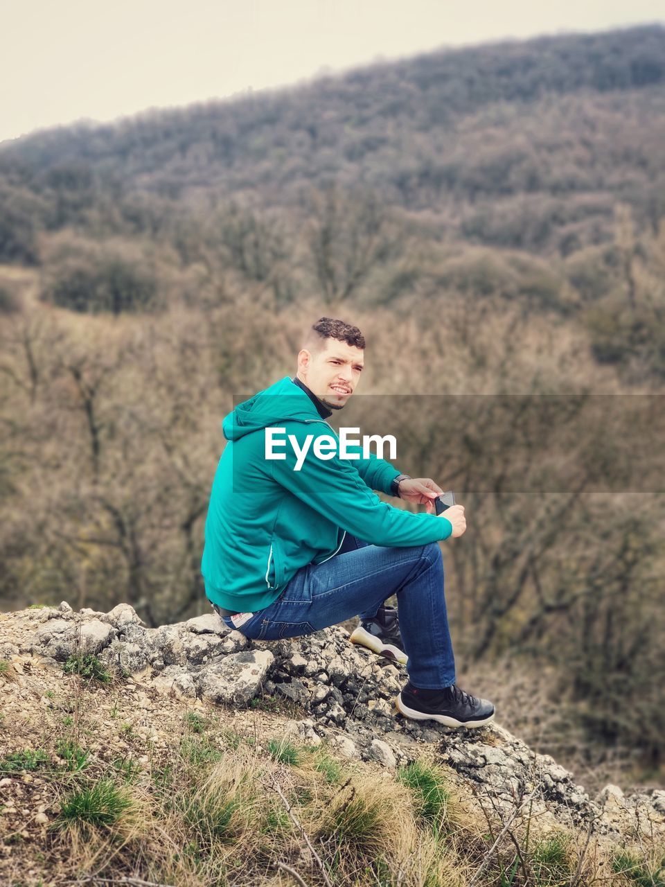 SIDE VIEW OF YOUNG MAN SITTING ON LAND AGAINST TREES