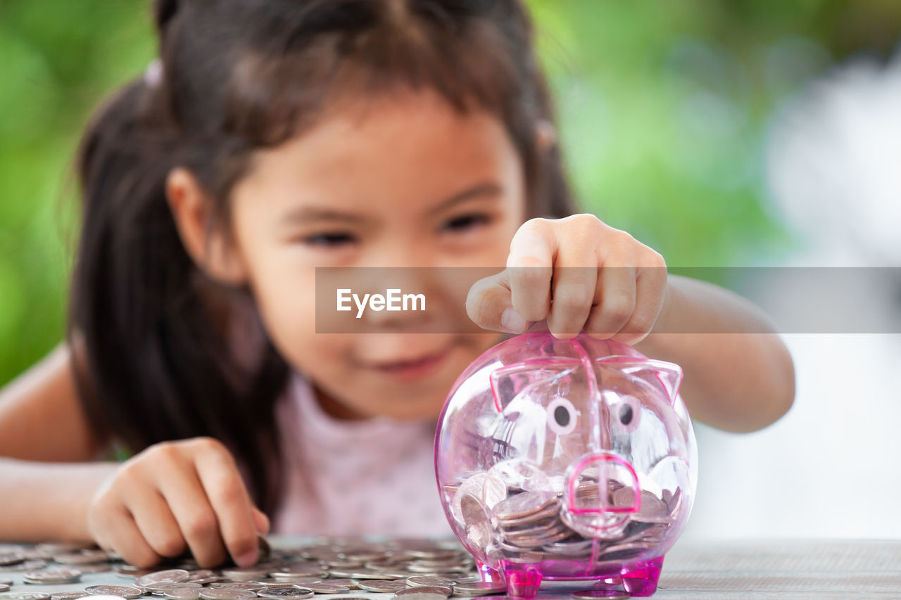 Girl putting coin in piggy bank at table