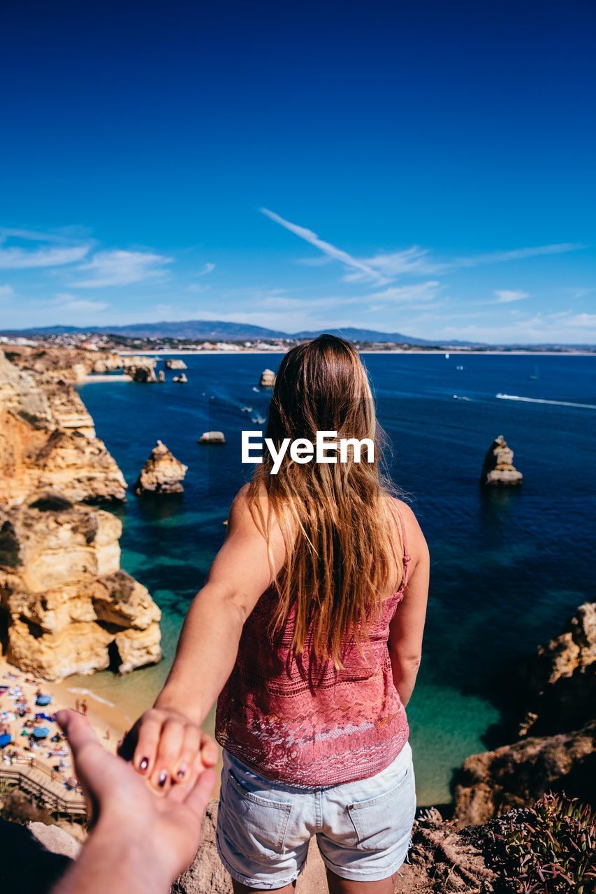 Cropped hand of man holding woman hand on cliff by sea