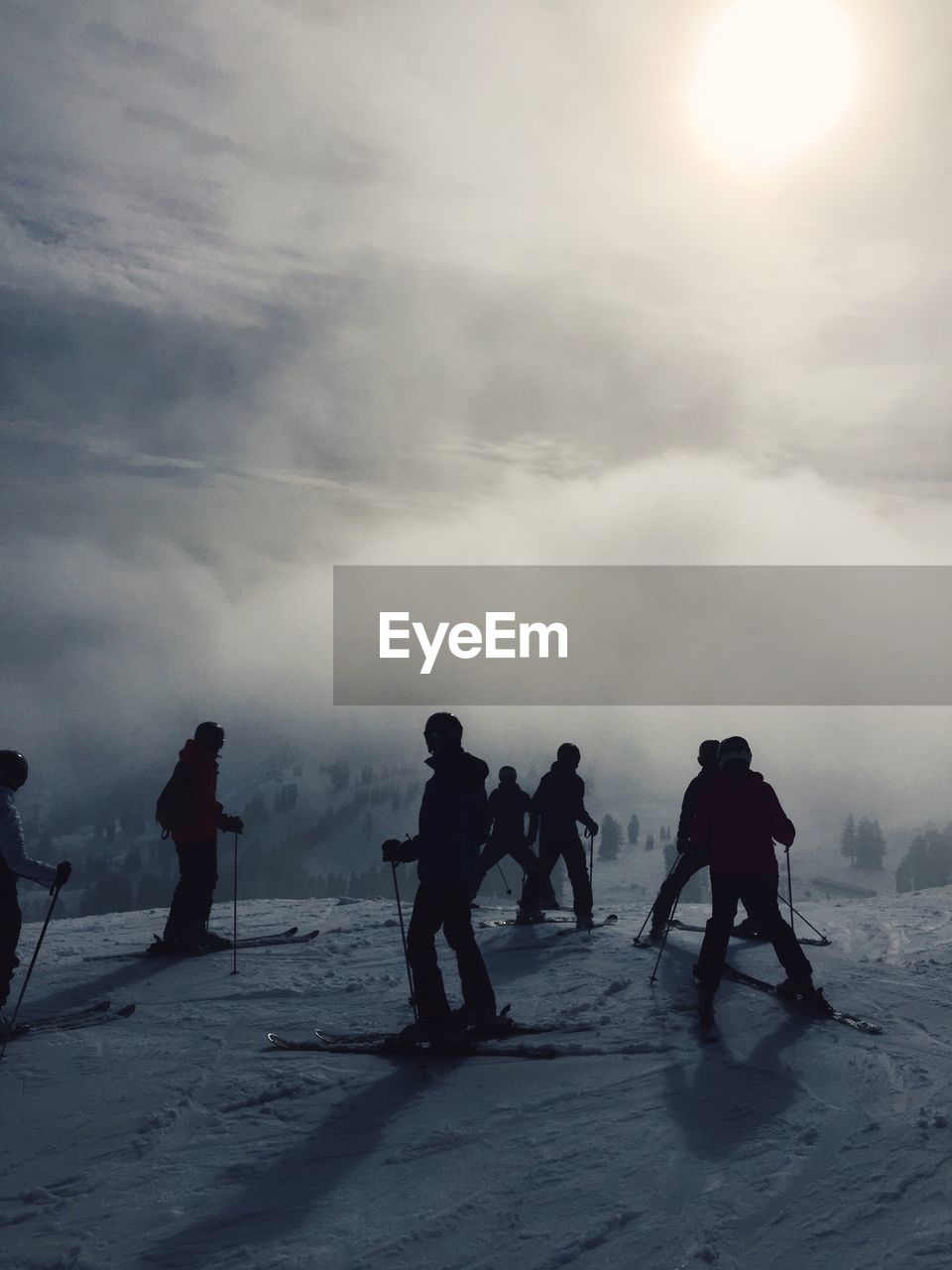 Silhouette skiers on snowcapped mountain against cloudy sky