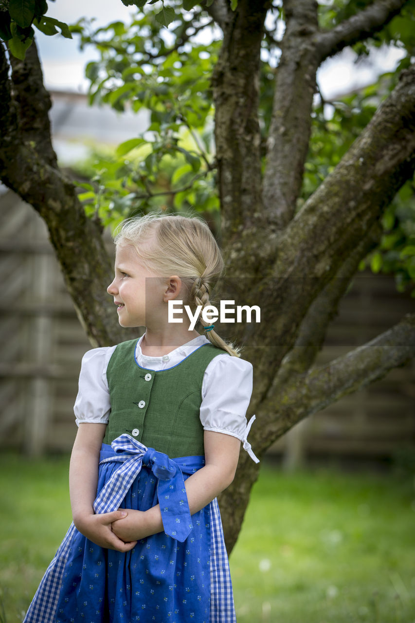 Cute girl looking away while standing against tree trunk