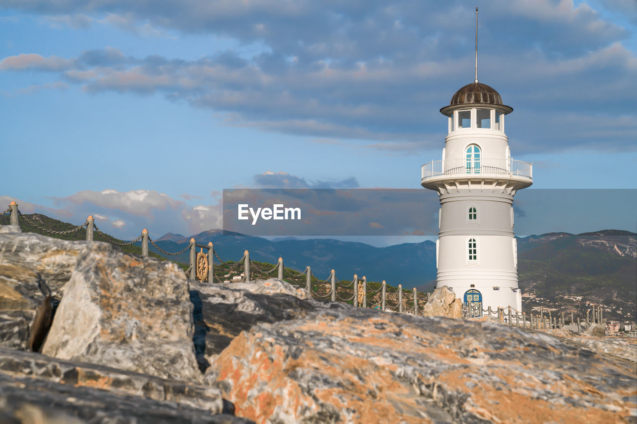 White port lighthouse on the background of mountains and sky and clouds.