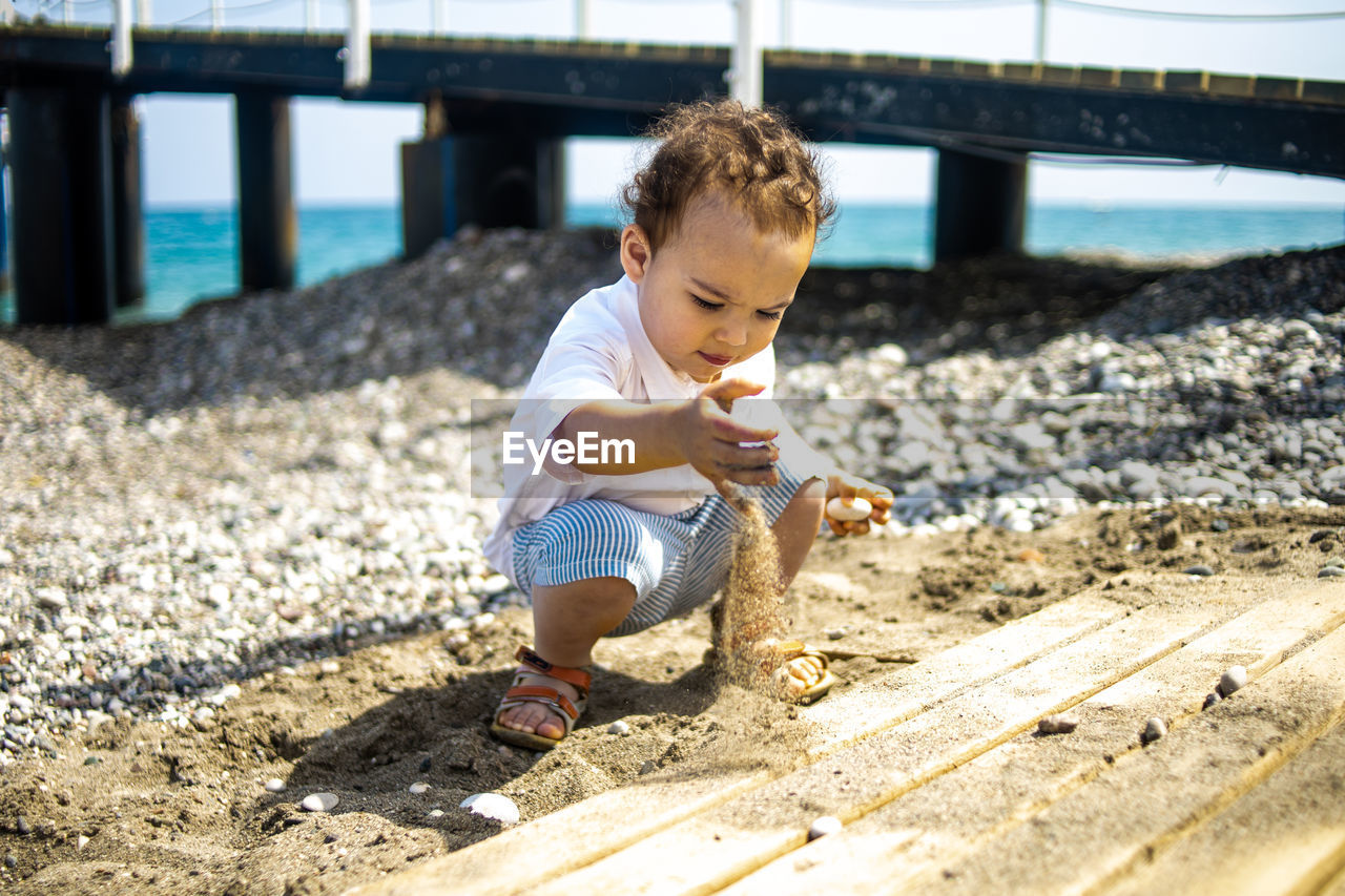 Happy toddler boy in white shirt and blue shorts on the beach