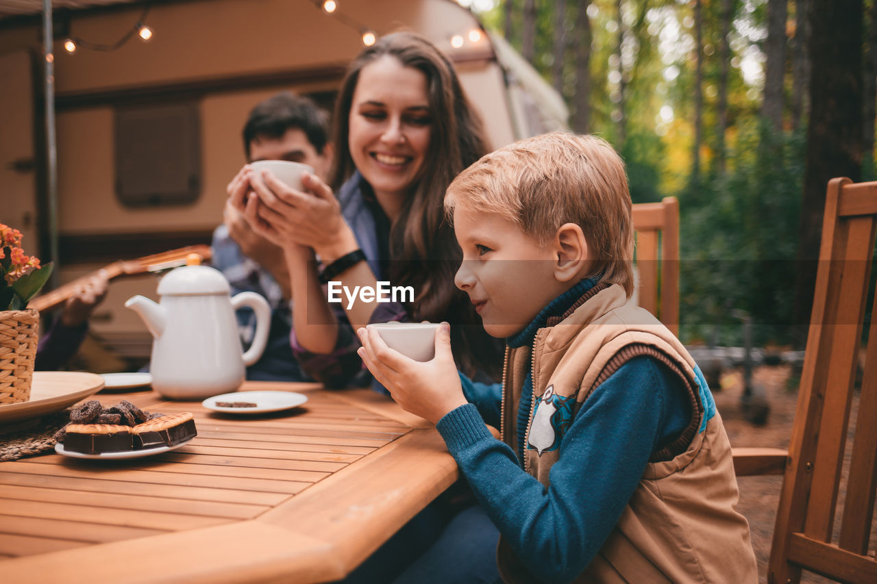 Happy family on camping trip relaxing in the autumn forest camper trailer. fall season outdoors trip