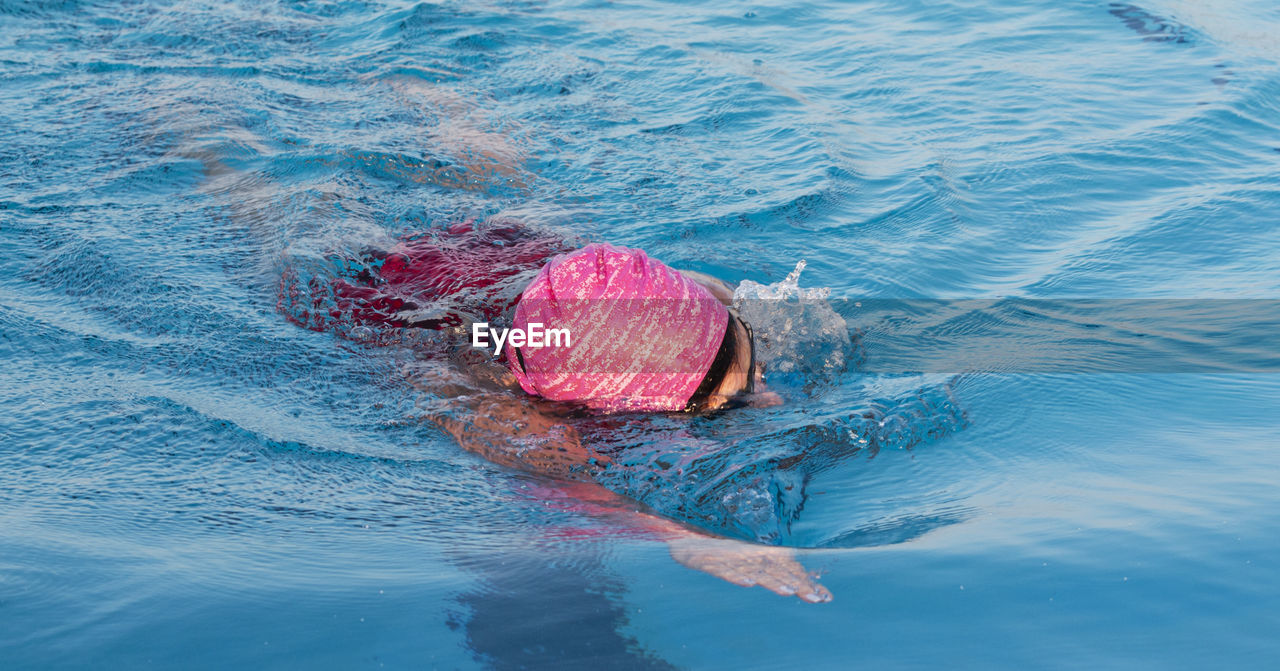 Close up of a women swimming laps directly at the camera in a pool wearing a pink bathing cap.