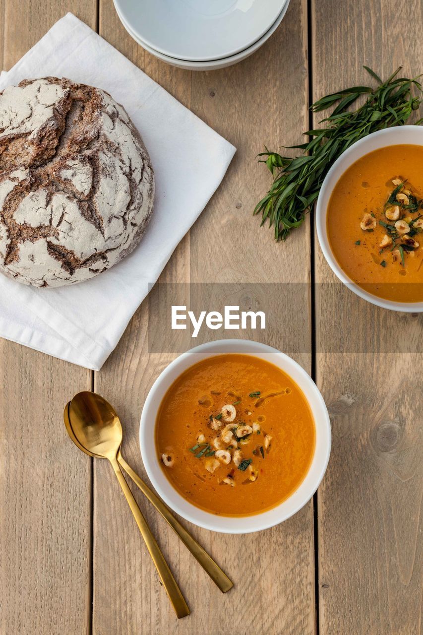 Directly above shot of pumpkin soup in bowls and bread on wooden table