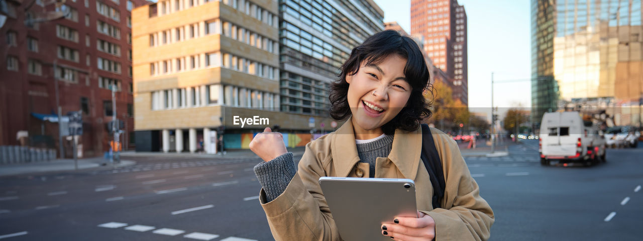 portrait of young woman using mobile phone while standing in city