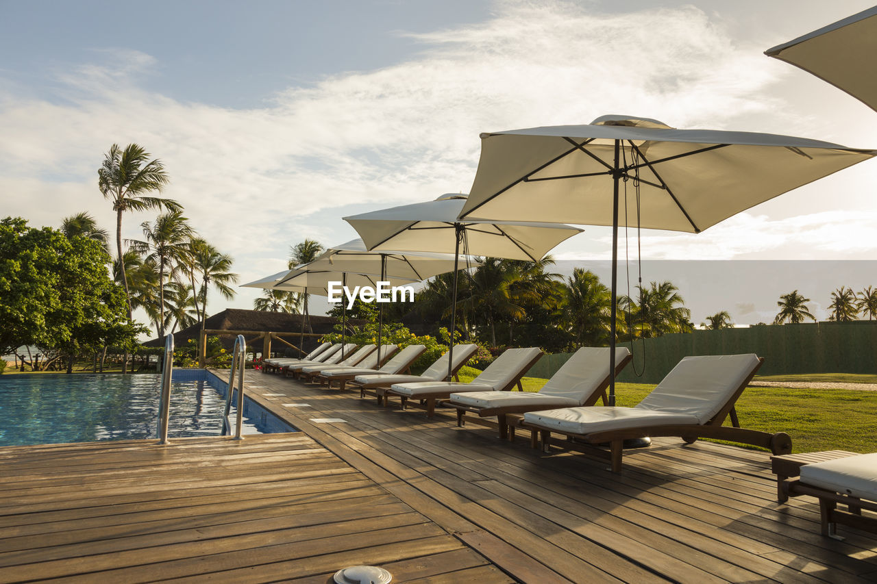 LOUNGE CHAIRS BY SWIMMING POOL AGAINST SKY AT RESORT