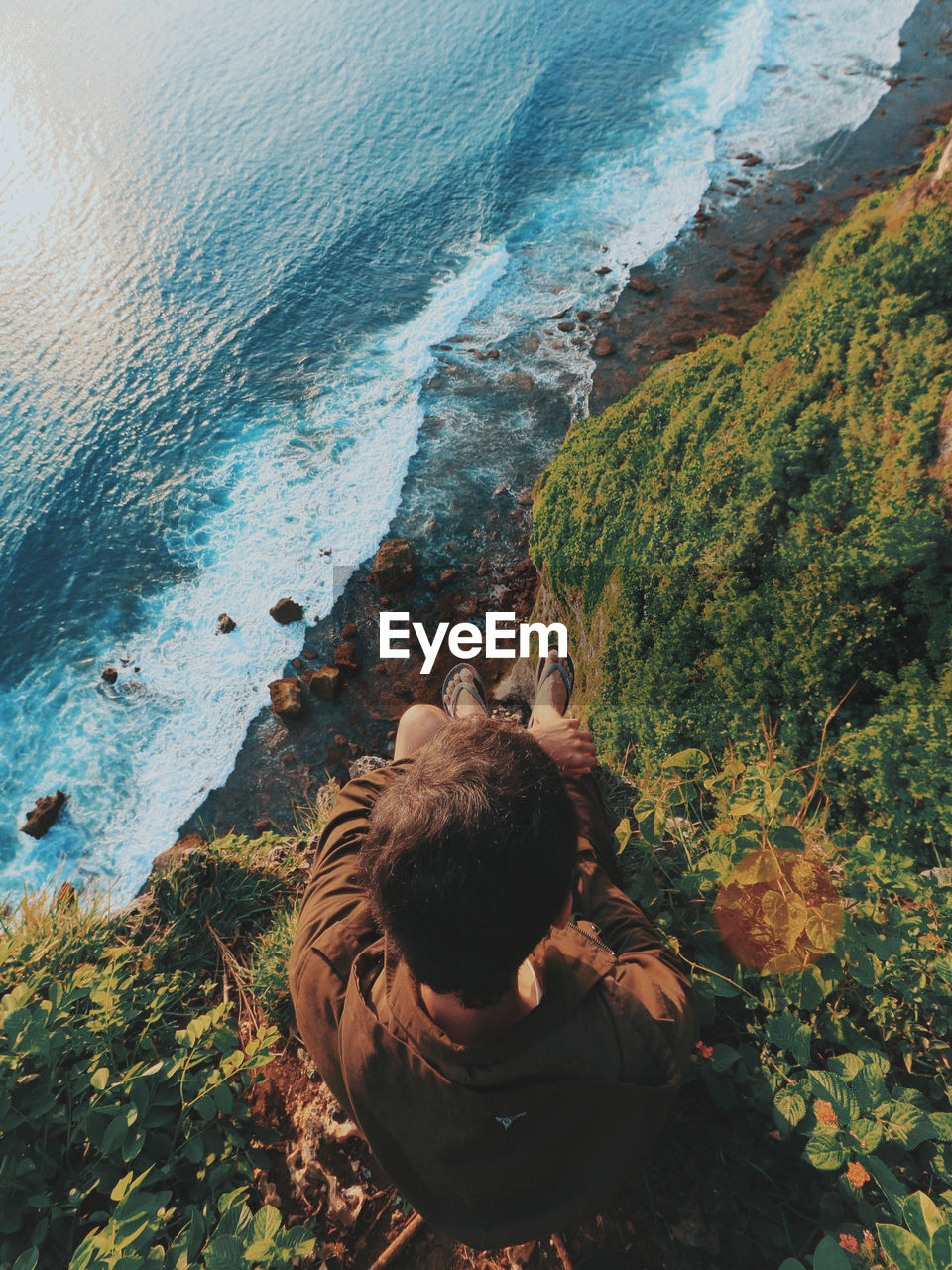 High angle view of man sitting on cliff by sea