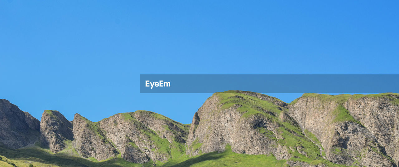 Low angle view of cliff against clear blue sky