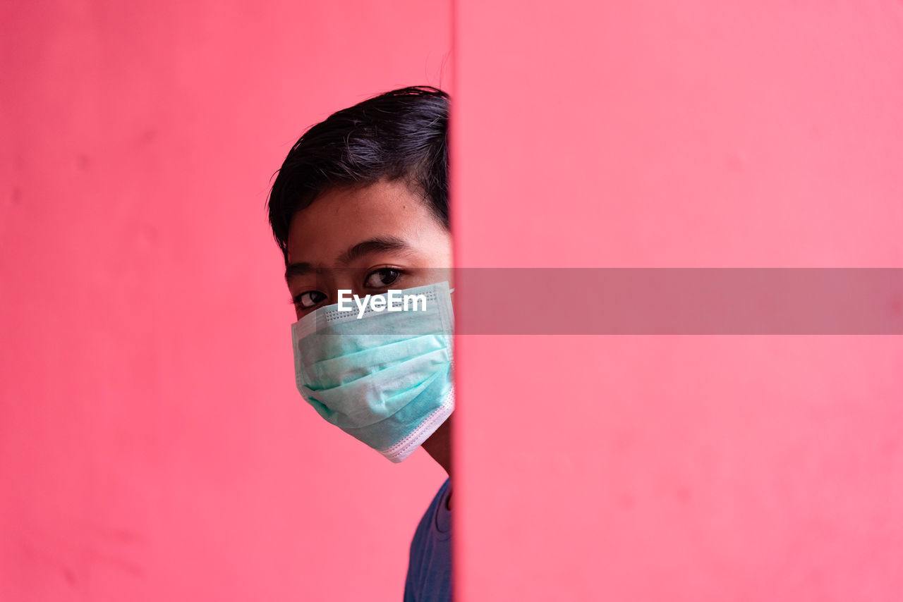 Portrait of young man against pink background with face mask