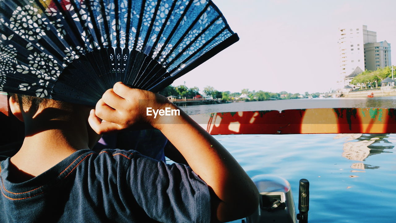 Rear view of child holding folding fan against sea in city