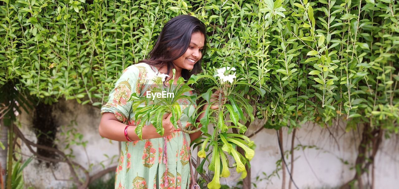 Smiling young woman standing by plants