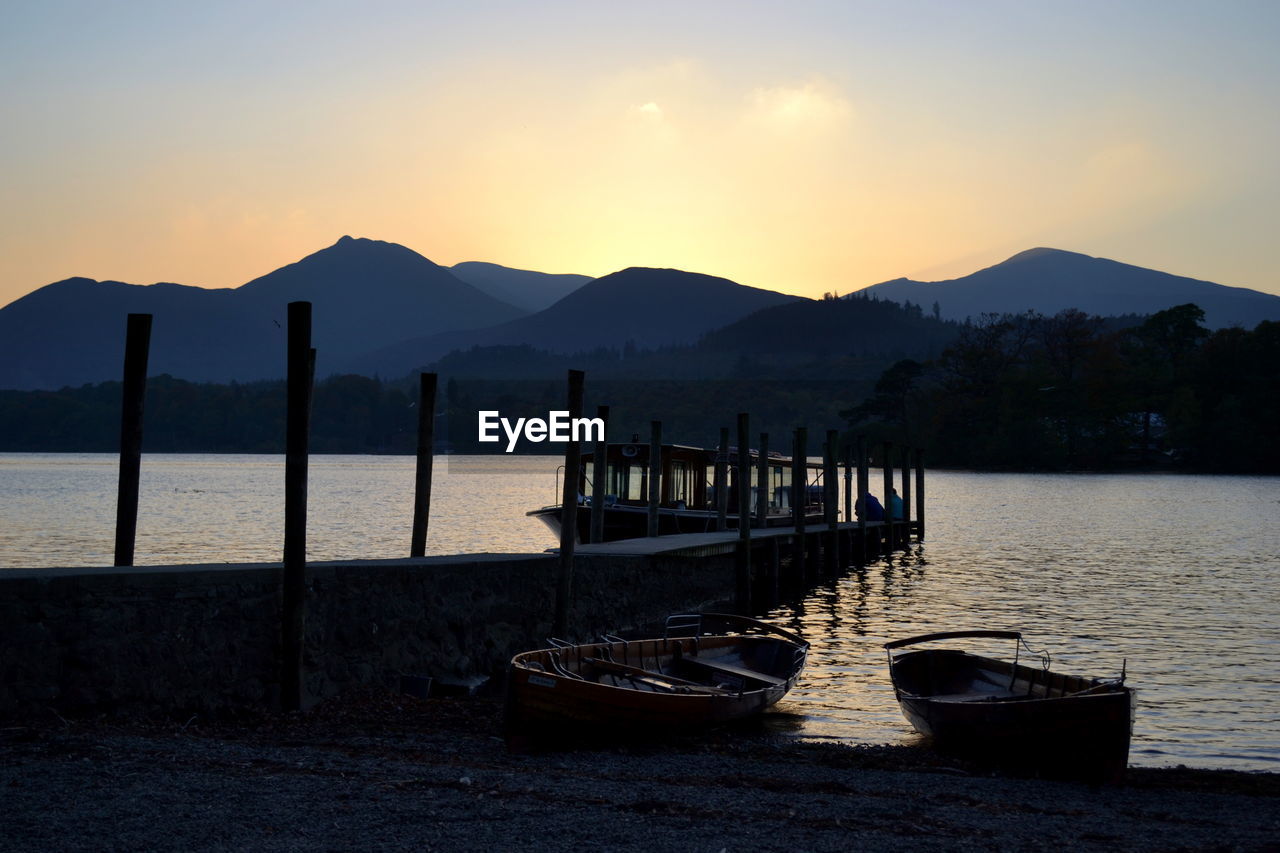 BOATS MOORED ON LAKE AGAINST SKY DURING SUNSET