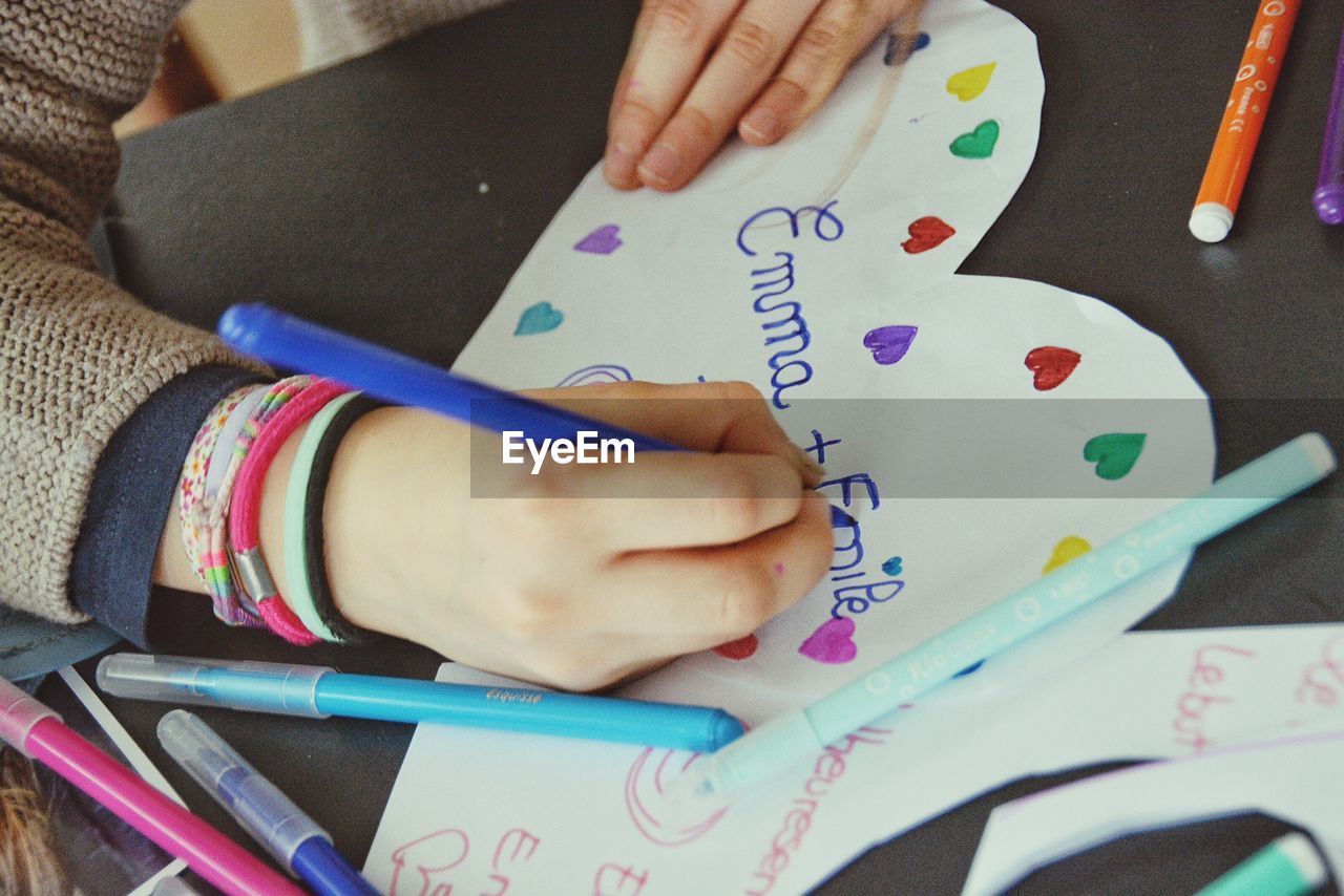 Cropped hand of girl writing on heart shape paper at home