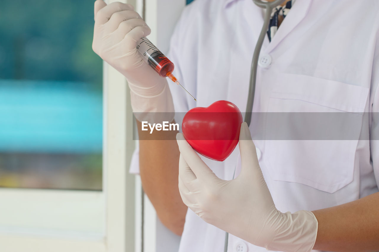 Midsection of doctor holding syringe over red heart shape