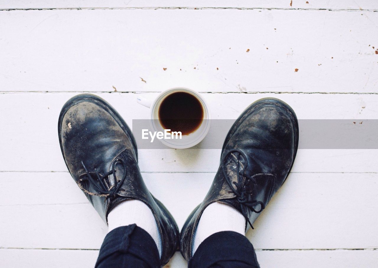 Low section of person standing by coffee cup on floor