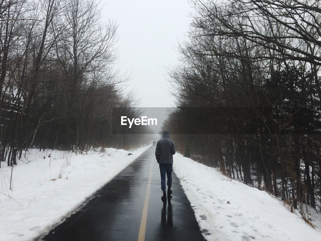 REAR VIEW OF MAN WALKING ON SNOW COVERED CANAL