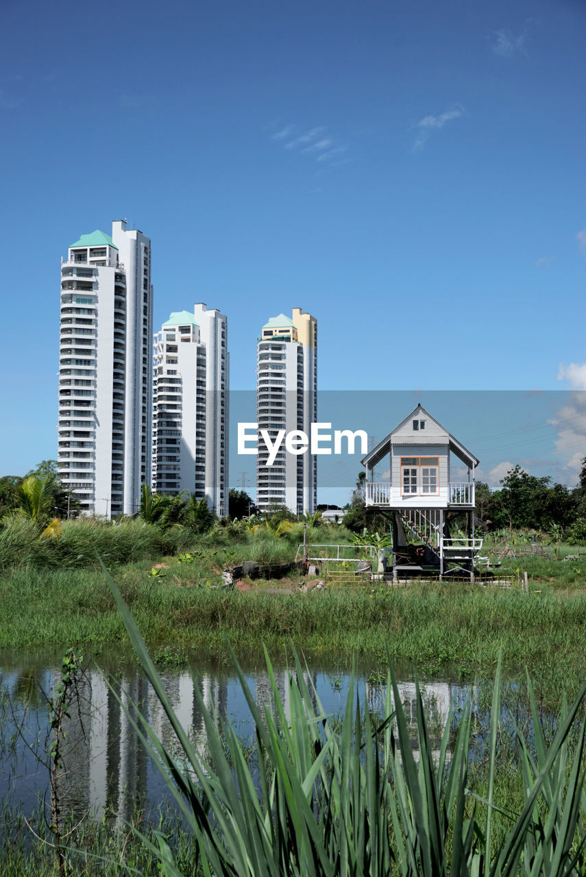 built structure, architecture, building exterior, building, sky, water, landscape, residential district, plant, nature, city, grass, no people, office building exterior, blue, horizon, house, lake, travel destinations, skyscraper, outdoors, day, tower, urban skyline, land, green, beach, growth, tree, residential area, travel, reflection, cloud, home, skyline, environment