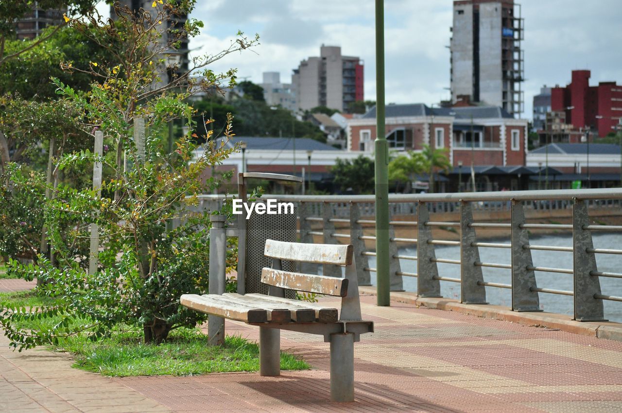 Bench on footpath by river in city