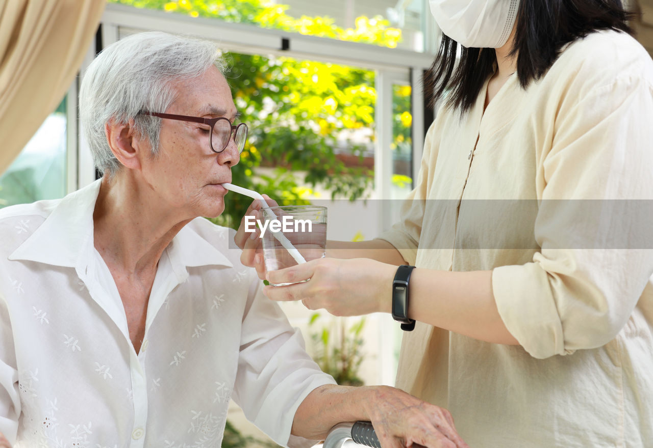 Midsection of nurse feeding water to senior woman