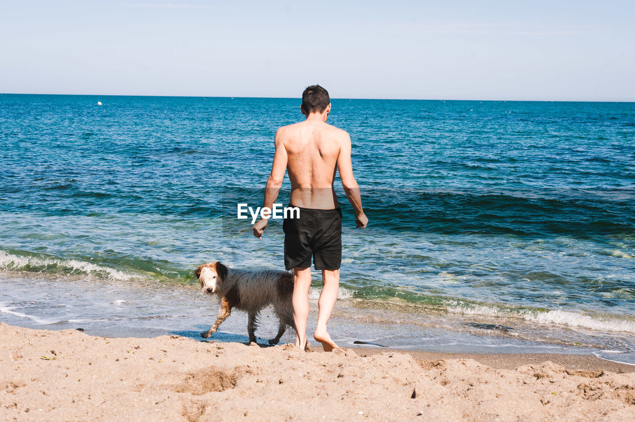 MAN STANDING WITH DOG ON BEACH