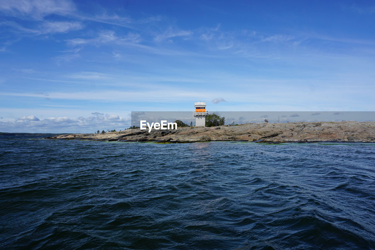 Lighthouse by sea against blue sky