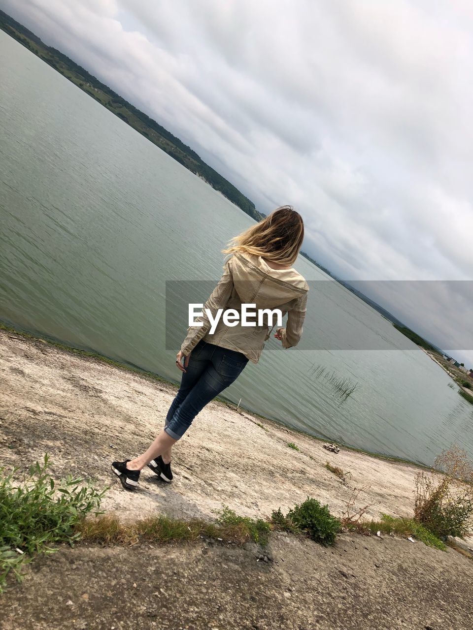 Rear view of woman standing at lakeshore against sky