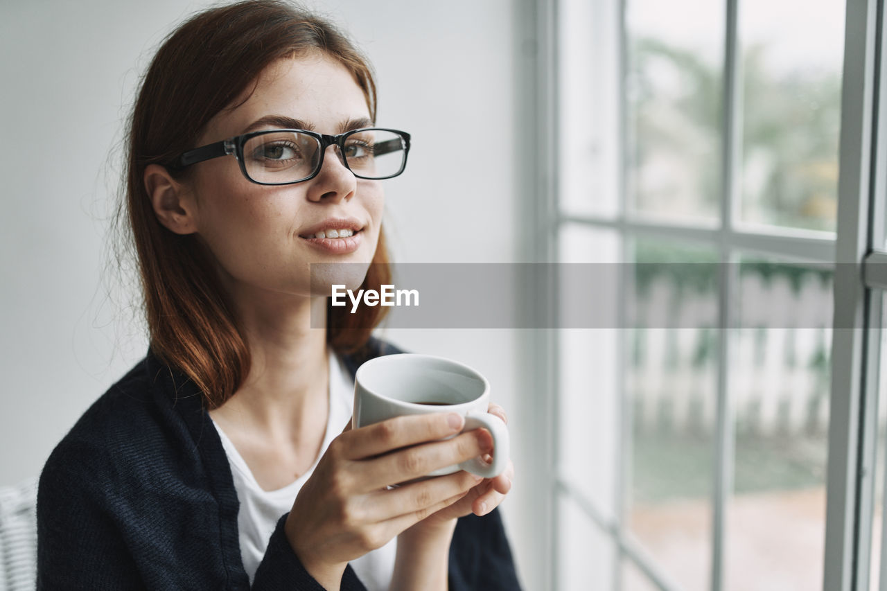 Portrait of young woman drinking coffee by window