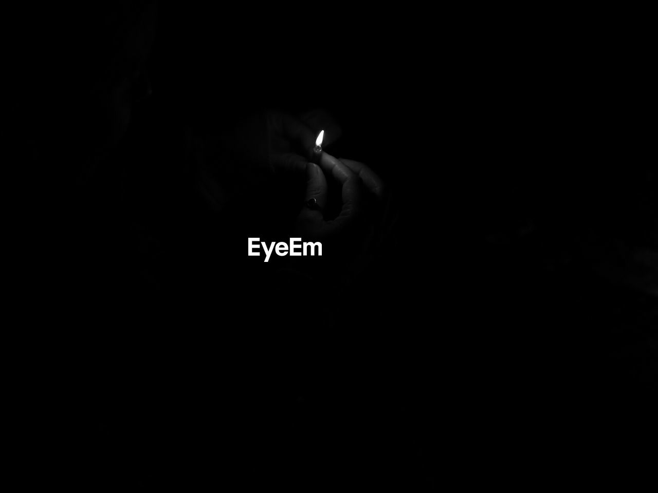 Cropped image of hand holding illuminated candle against black background