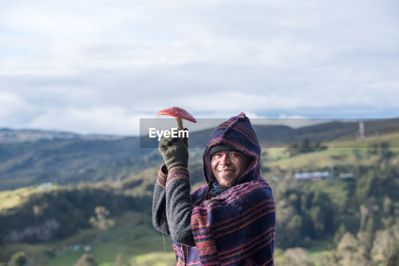 Colombian native american man in traditional clothing with mushroom as umbrella against panorama