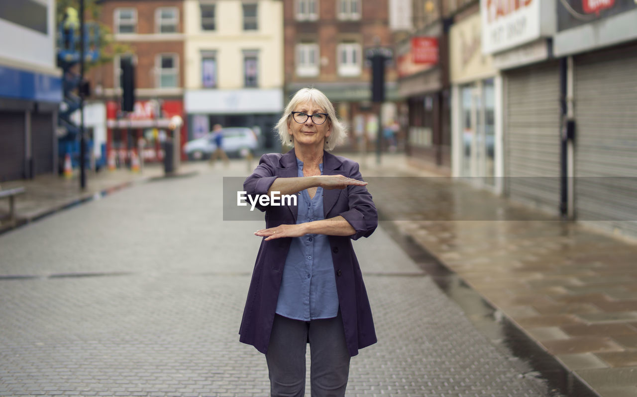 Portrait of woman gesturing while standing on footpath against buildings