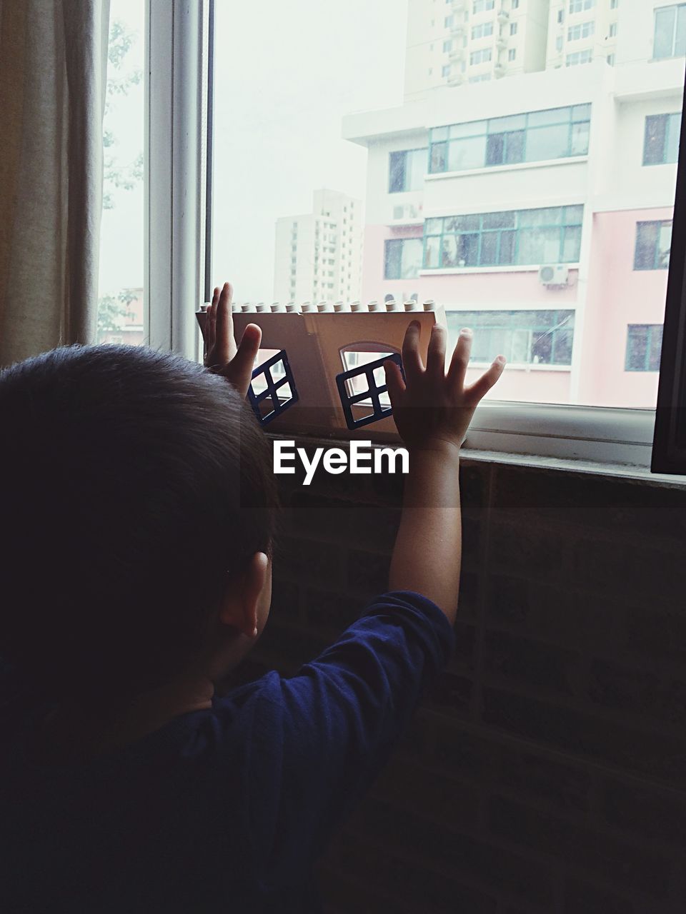 Rear view of child with toy at window sill